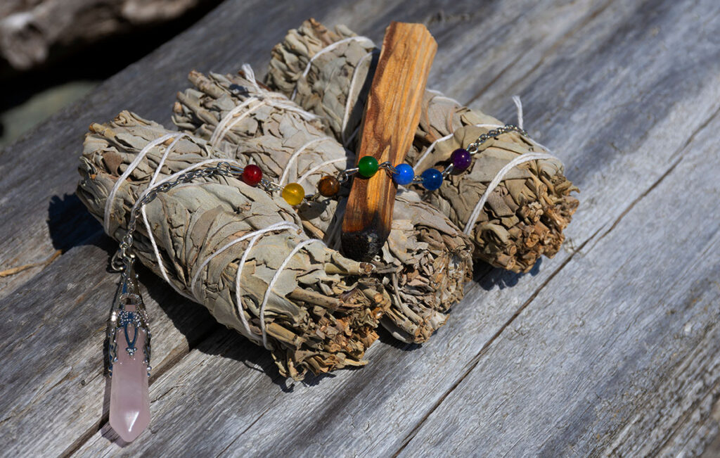 Pendule en quartz rose posé à côté de feuilles de sauge et de palo santo pour se faire purifier